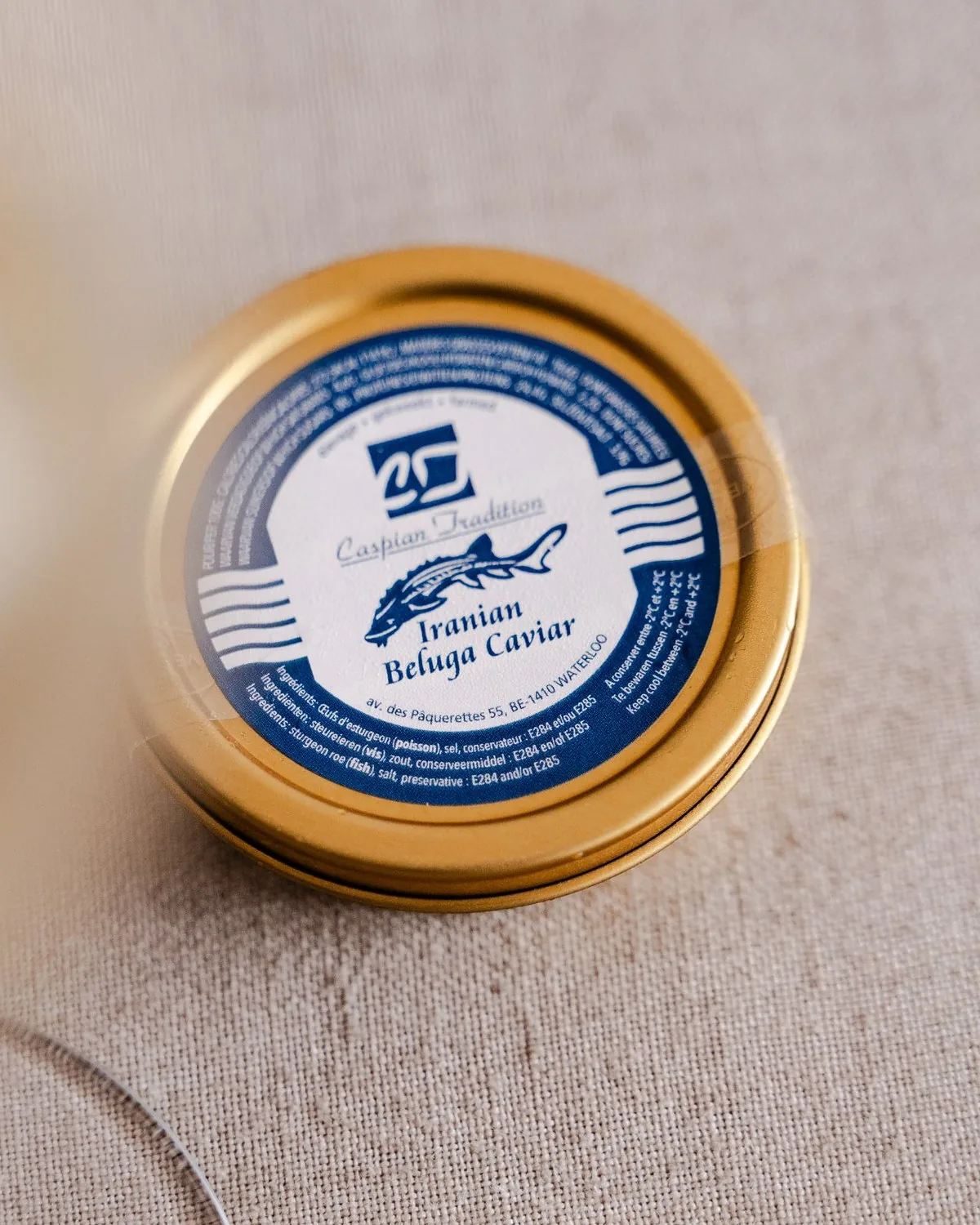 A tin of Caspian Tradition Iranian Beluga caviar on linen, beside a glass